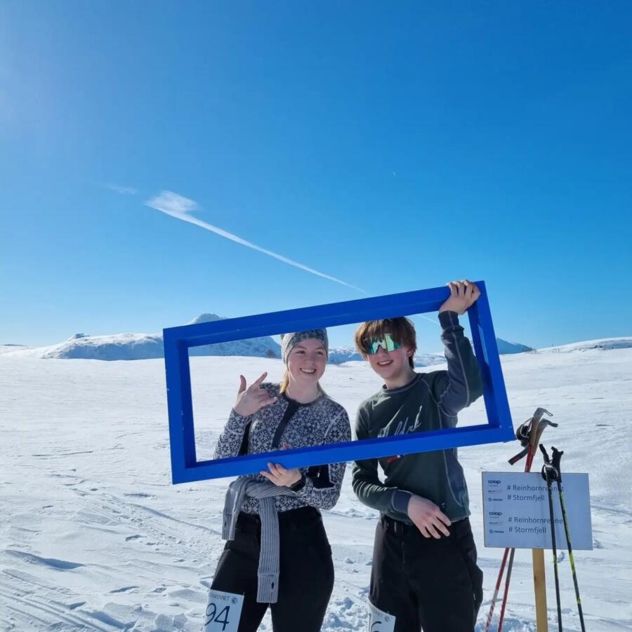 To unge deltakere holder opp en blå fotoramme i snøen på Beiarfjellet